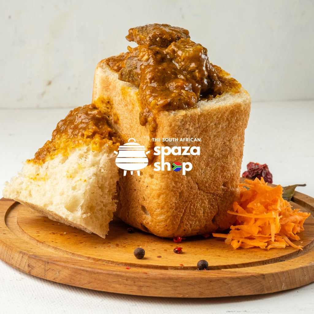 “Authentic South African bunny chow filled with spicy curry, served in a hollowed-out loaf of bread on a wooden board with grated carrot garnish — The South African Spaza Shop.